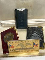 Lot contents showing two 1939 miniature Masonic books, black cigarette holder, Social Security card, and dog tags.