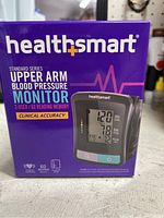 Front view of the product box showing brand name, product type, 2-user capability, 60 reading memory, and clinical accuracy claim, including an image of the digital monitor displaying blood pressure and pulse readings.