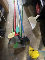 Top-down view of four brooms laid on the floor alongside white dustpan