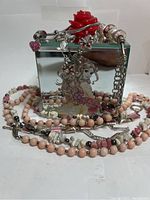 Front view of the mirrored jewelry box with Disney princess decal and rose handle surrounded by assorted pink and white bead necklaces and bracelets.