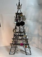 Front view of black Eiffel Tower jewelry rack with numerous pairs of earrings and rings displayed on hooks and cross bars.