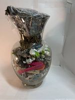 Side view of clear glass vase jar showing vintage jewelry inside including chains, beads, and fabric accessory.