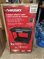 Photo showing the boxed Husky 2-shelf utility cart with product information and branding visible on packaging.