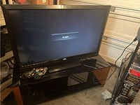 Vizio TV on dark red wood and glass entertainment center with cords and remote on top.