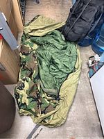 Large military sleeping bag with camouflage exterior laid out on the floor, showing olive green insulated interior.