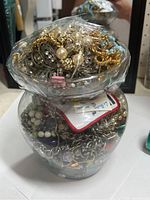 Photo of jar filled with various gold-tone metal chains, faux pearl jewelry, and decorative clips visible at top.
