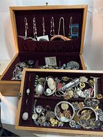 Open jewelry box showing top layer with hanging bracelets and front tray filled with assorted vintage jewelry.