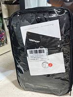 Front view of sealed black heated vest inside transparent zippered fabric case showing tags and Power Bank branding.