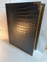 Front view of a brown alligator skin texture leather secret hiding book with metal corner accents on top and bottom right corners.