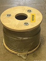 Large wooden spindle loaded with thick silver braided wire, partially wrapped in plastic.