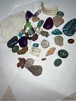 Overview of various stones and minerals including quartz, turquoise, amethyst, and fossil pieces spread on a white surface.