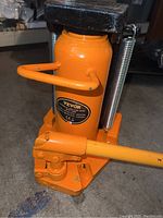 Front view of orange hydraulic cylinder, pump handle attached