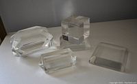 Four clear Lucite pieces displayed on a white surface under diffuse lighting.