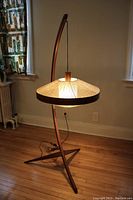 Full view of the lamp lit in room showing arc stand, base and shade