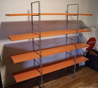 Front view of retro orange shelving unit showing all four shelves and metal frame.