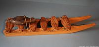 Side view of wooden sled showing six leather strapped crossbars and soapstone seal figurine attached