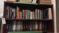 Two shelves filled with a diverse collection of books covering self help, gardening, inspirational themes, and novels by known authors.