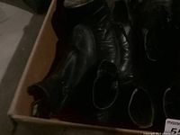 Box with several pairs of black leather men's boots and shoes, showing wear and used condition.