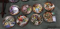 Eight collector plates laid out on floor, showing various floral designs in a set called Flowers of Your Garden series by Vieonne Morley, each plate approximately 8.5 inches diameter.