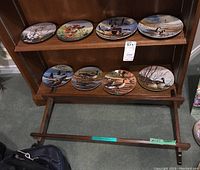 Eight collector plates displayed on wooden display stand with two shelves, showing various wildlife scenes primarily waterfowl and nature.