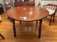 Front angle view of the round wood dining table on hardwood floor, showing turned legs and surface wear.