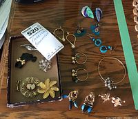 Photo showing assortment of earrings, pins, and a bracelet arranged on a wooden surface and in a small box.