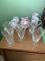 Six clear glass goblets with floral etching visible, one with chip