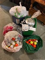 Five bags filled with assorted mostly used golf balls in white, orange, and yellow colors, and a Wilson ladies golf glove resting on a green tote.