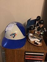 Blue Jays replica batting helmet and two bobblehead figures displayed on wooden shelf above CDs