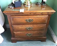 Front view of wooden night stand showing three drawers with decorative brass pulls and oak finish.