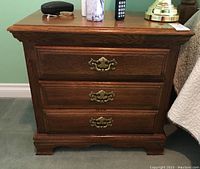 Front view of the Athens Furniture night stand showing three drawers with ornate brass handles.
