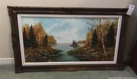 Full view of framed painting showing autumn trees and water scene, including frame condition and signature area.