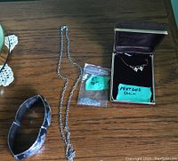 Sterling and gold jewelry including bracelet, chains, and pendant in box photographed on wooden surface.