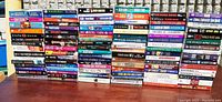 Image shows multiple stacks of soft cover fiction books with colorful spines and assorted authors.