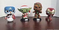 All four Funko Pop figures together showing Captain America snowman, Yoda in Santa outfit, Chewbacca with Christmas lights, and Iron Man.