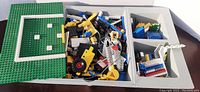 Divided grey plastic storage tray holding assorted LEGO pieces and green baseplates
