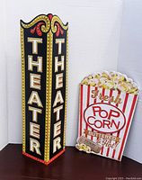 Photo showing both the metal theater sign and the wooden popcorn sign side by side