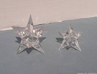 Two Rosenthal 9-point star crystal candle holders, one larger and one smaller, placed on a surface showing light reflections and clear cuts.