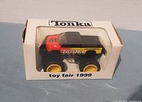 Front view of Tonka toy truck in original white box with clear window, showing 'Tonka' and 'toy fair 1999' text on box.