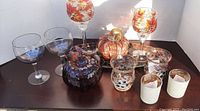 Photo showing the full lot of candle holders and fall decorative pumpkins on a dark wood surface. Includes glass holders with leaf designs, glass pumpkins, a decorative tray and ceramic votive holders.
