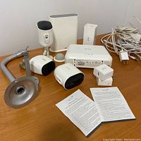 Overview of three Arlo cameras, base stations, adapters, mounting brackets, power cables, and manuals on wooden surface