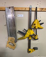 Photo of two yellow Wolfcraft furniture clamps and rusty back saw hanging on a wooden strip.