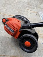Side view of the Black and Decker Edge Hog edger lying on a concrete surface, showing the orange motor housing with Black and Decker label and wheels.