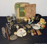 Overview of the lot arranged on a black surface showing various collectibles including jewelry, figurines, glassware, and decorative items.