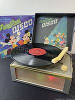 View of the Mickey Mouse Disco record player with a vinyl record on the turntable and disco-themed album cover behind.