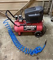 Front perspective showing red tank, black motor cover, gauges, handle and coiled hose extended on floor