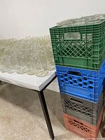 Wide view of many clear Mason jars arranged on a white table and stacked in colored plastic crates.