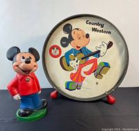 Photo of vintage Mickey Mouse plastic bank in red shirt and blue pants standing next to the country western drum with colorful Mickey image.