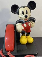 Full frontal view of the vintage Mickey Mouse phone showing Mickey figure with red handset and coiled cord on black base.