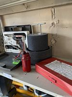 Weller soldering iron in molded foam case, red oil can, belt sanding paper rolls, and red metal case on shelf